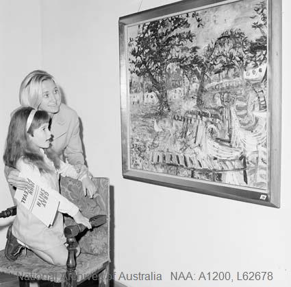 Black and white photograph of an unidentified woman and young girl at the 1967 preview exhibition in Henri Souillac's Canberra home, looking at a large framed landscape painting, the girl seated on a carved chair holding the exhibition programme.